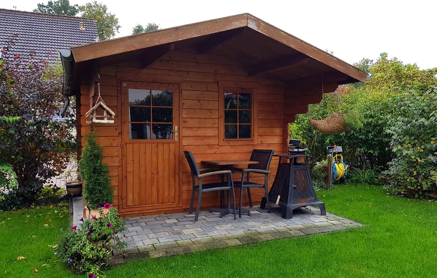 Ein Holz-Gartenhaus mit Gartenmöbeln davor, ideal für stilvolle Gartenbereiche.