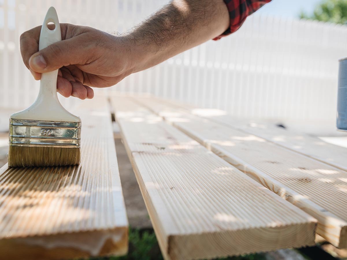 Auftragen von Holzöl mit Pinsel auf Terrassendielen zum Schutz der Oberfläche