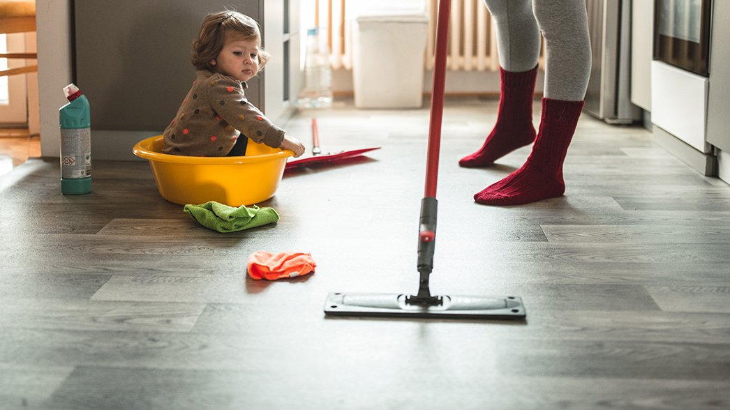 Mutter reinigt Boden während Kind spielt 